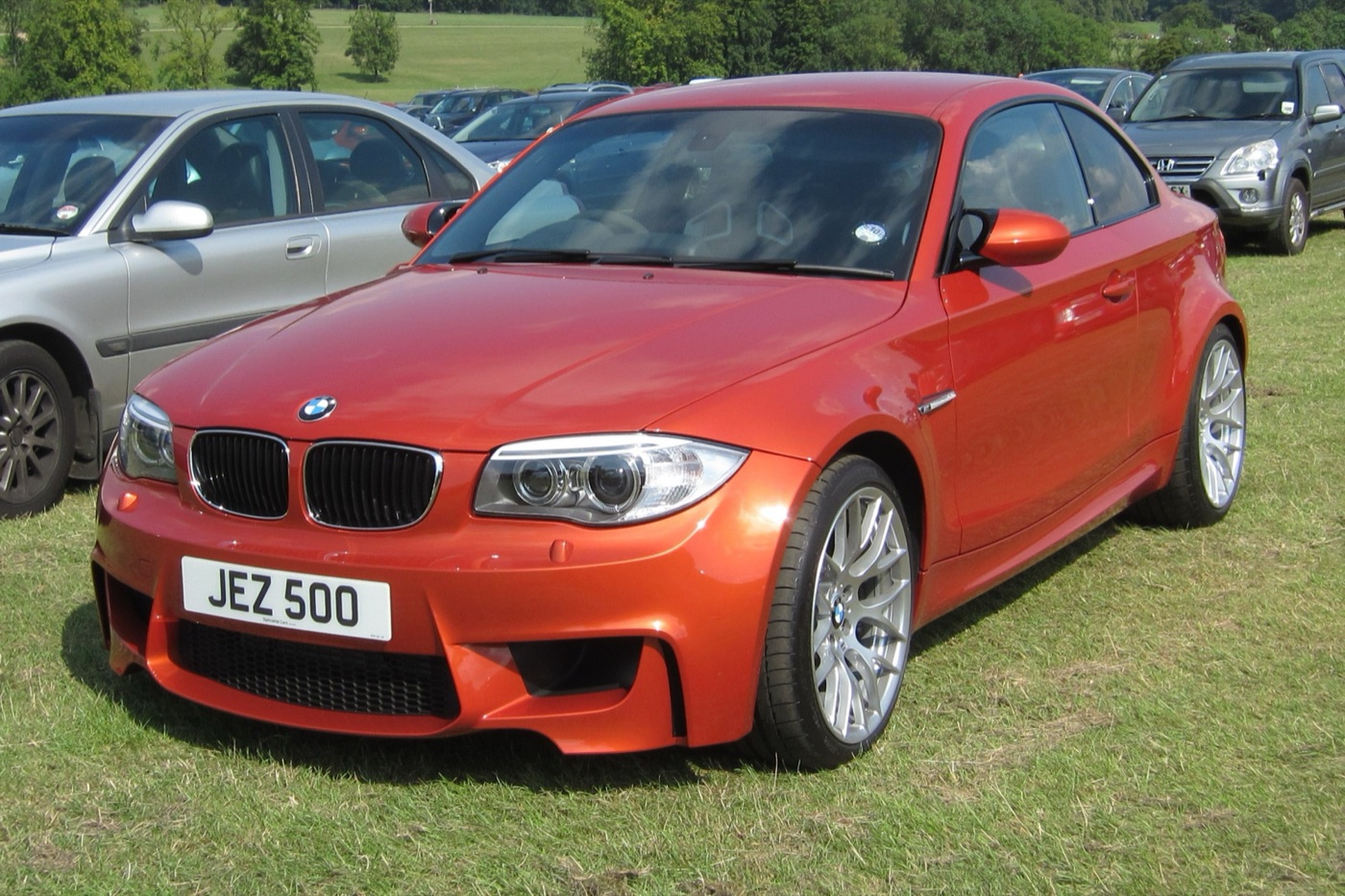 Valencia Orange BMW 1M with a UK private number plate parked on grass at a car show